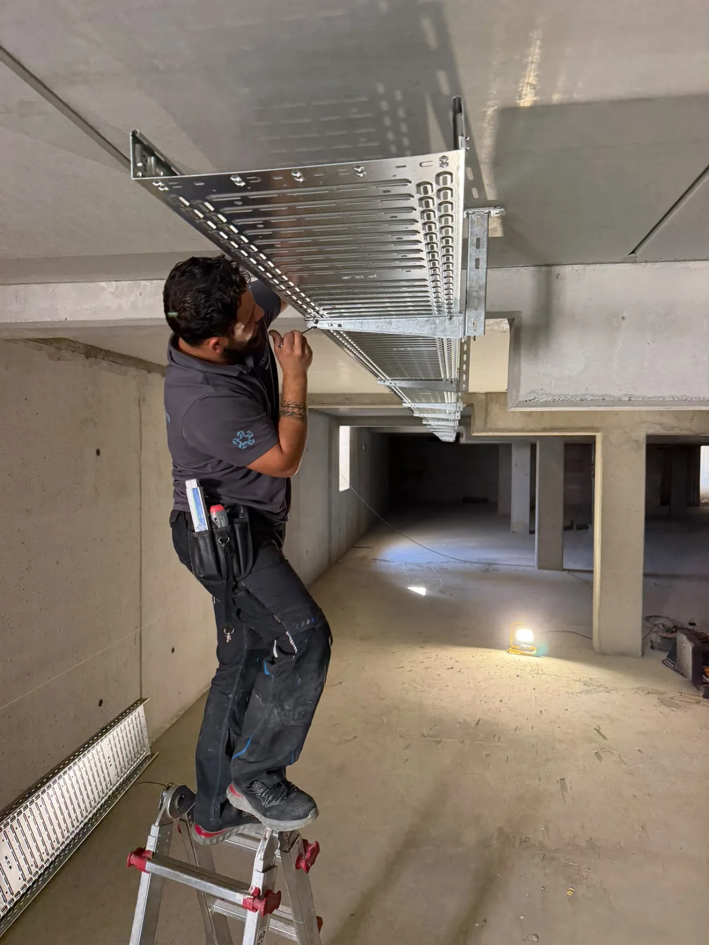 HausEtage-Monteur montiert eine Kabeltrasse an der Decke einer Tiefgarage im Rohbau