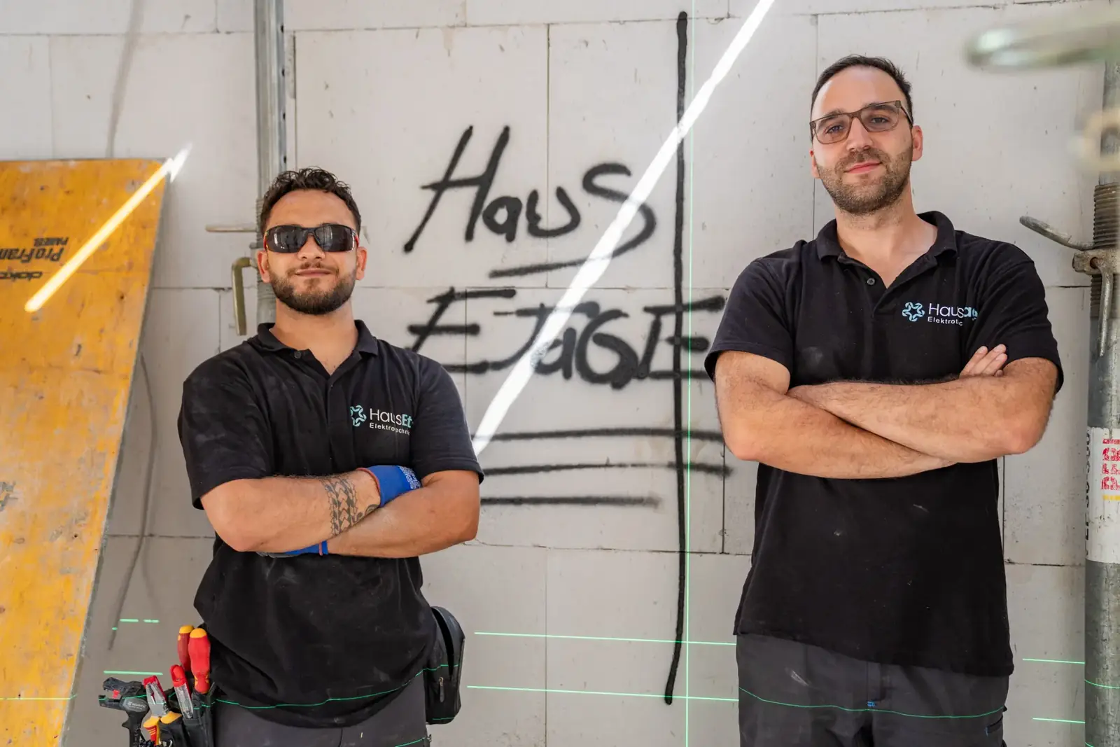 Zwei Elektriker von HausEtage vor einer Wand mit HausEtage-Schriftzug
